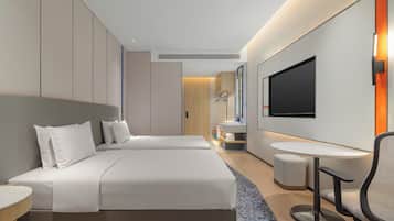 A modern hotel room with a large bed, a small desk, a chair, a TV, and a bathroom visible through a door.