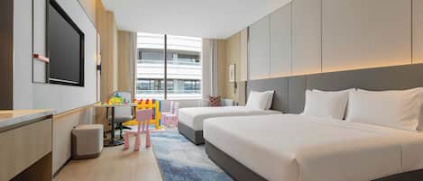 Habitación de hotel con una cama grande, un escritorio con silla, un televisor y vistas a la ciudad a través de amplios ventanales.