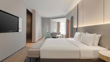 Una habitación de hotel moderna con una cama grande, un televisor de pantalla plana en la pared, un pequeño espacio de descanso con una silla y una mesa, y una estructura decorativa tipo tienda.