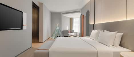 Una habitación de hotel moderna con una cama grande, un televisor de pantalla plana en la pared, un pequeño espacio de descanso con una silla y una mesa, y una estructura decorativa tipo tienda.