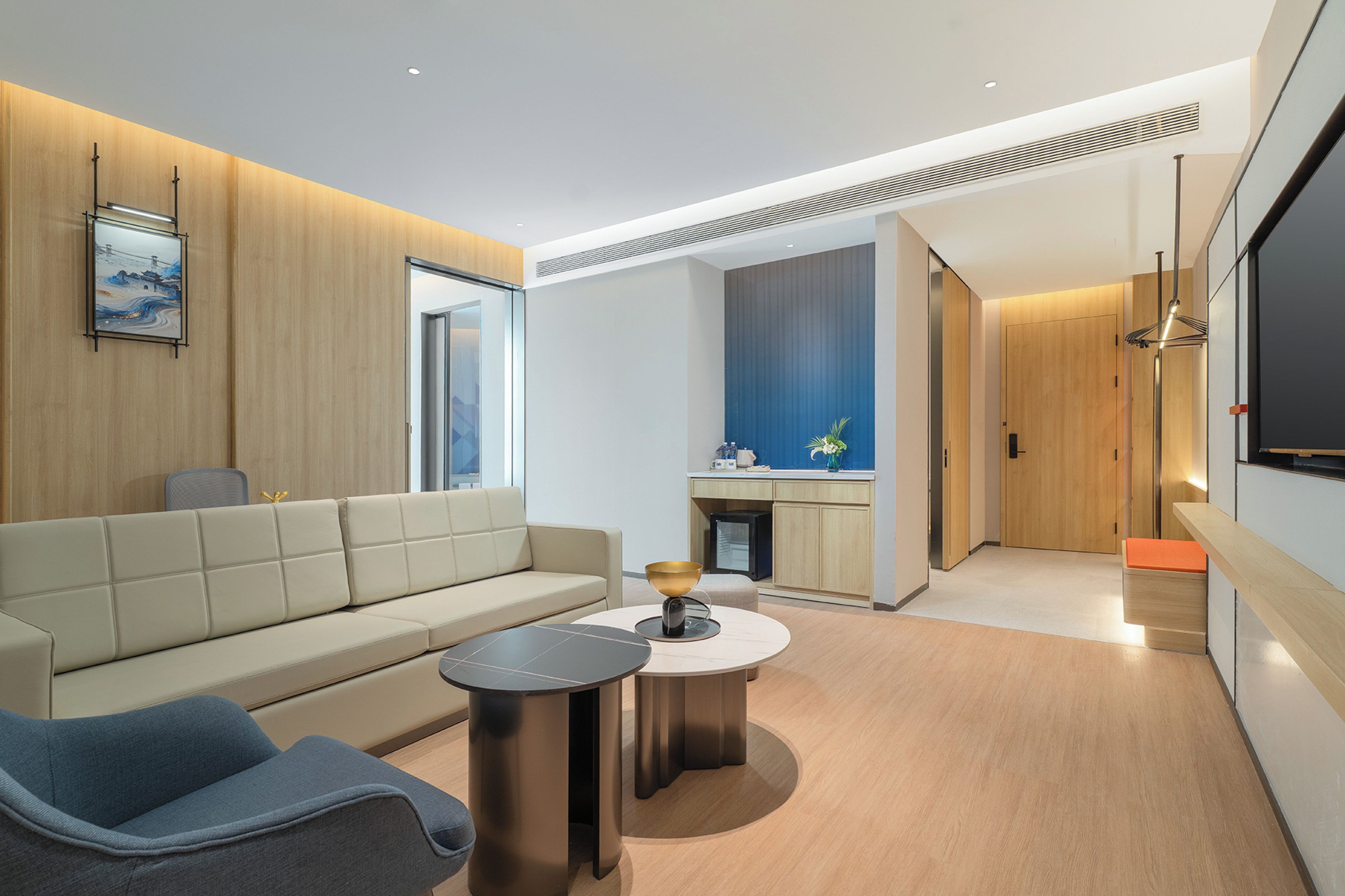 Ein modernes Wohnzimmer mit einer Couch, zwei Beistelltischen und einem Couchtisch. Durch einen offenen Durchgang ist eine Küche mit Spüle und Schränken erkennbar.