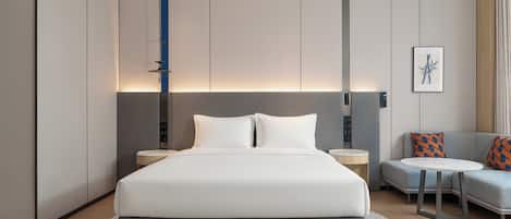 A modern hotel room with a large bed, bedside tables, a small sofa, and a patterned rug.