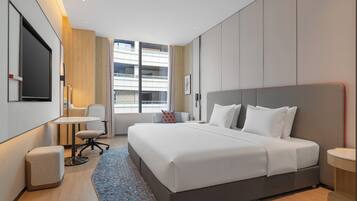 A modern hotel room with a large bed, a desk, and a view of a building through the window.
