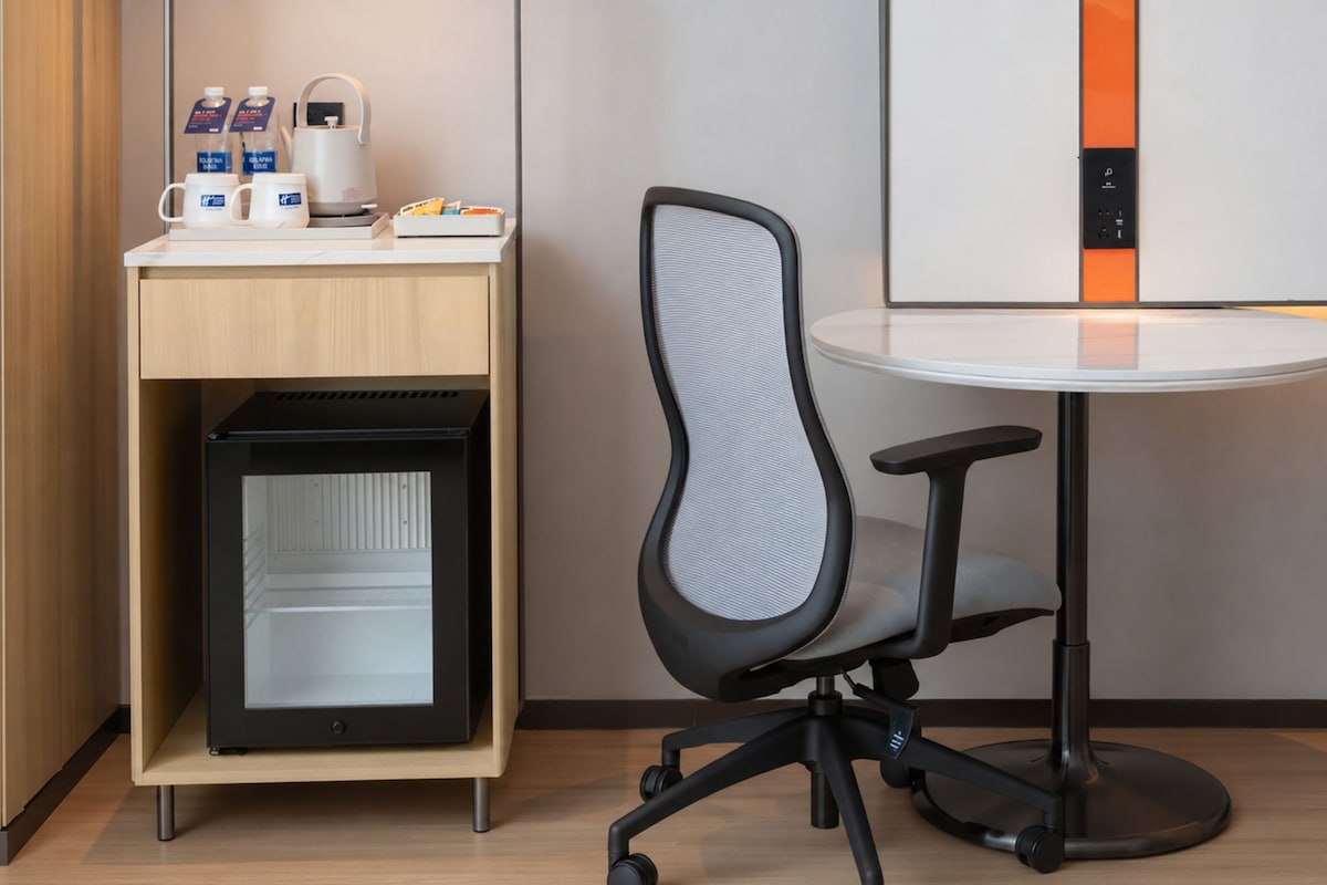 A modern office chair with a mesh backrest and a black base, positioned next to a white table with a glass top.