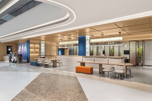 Un lobby moderno de hotel con una recepción, zonas de estar y un amplio espacio abierto.