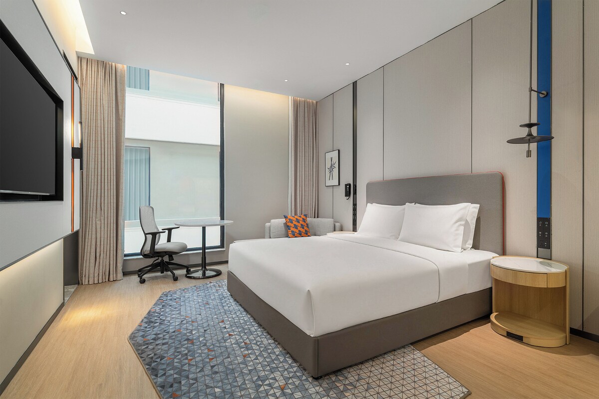A modern hotel room with a large bed, a desk, and a chair.