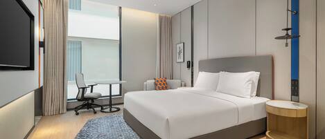 A modern hotel room with a large bed, a desk, and a chair.