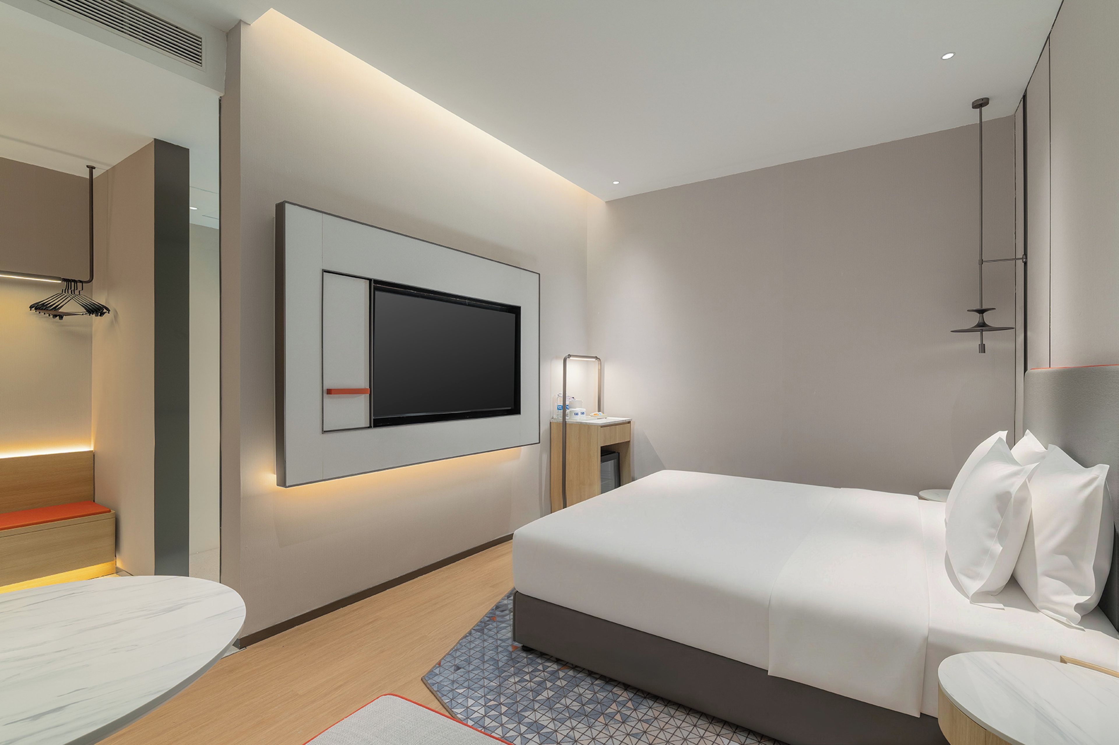 Ein modernes Hotelzimmer mit einem großen Bett, einem flachbildfernseher an der Wand, einem Nachttisch und einem kleinen Schreibtisch mit Lampe.