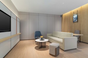 Una habitación moderna y luminosa con un sofá, una pequeña mesa redonda, una silla azul y un televisor montado en la pared.
