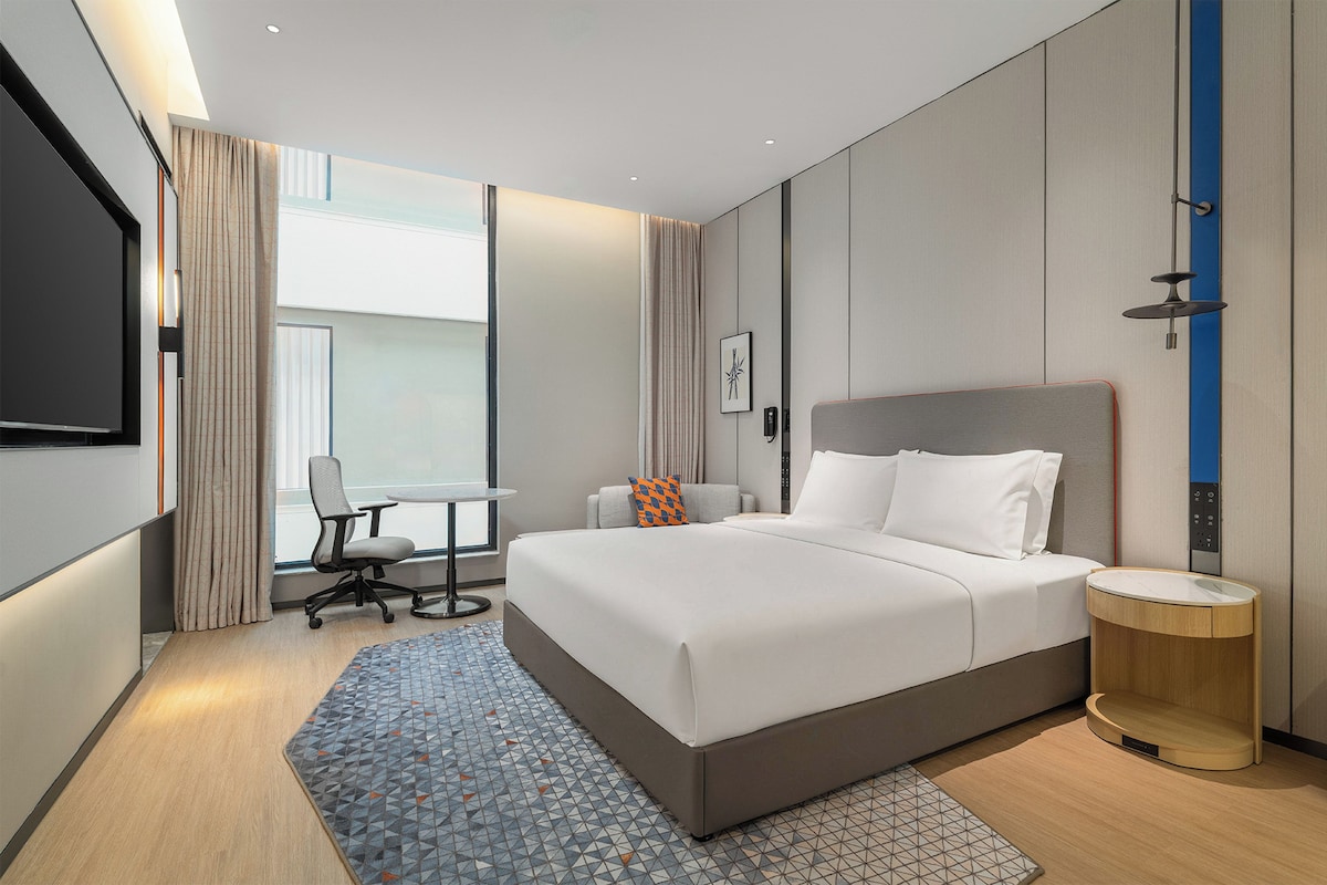 A modern hotel room with a large bed, a desk, and a chair.