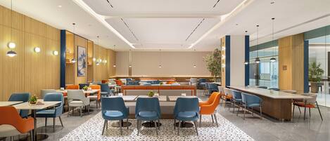 Un comedor moderno con mesas y sillas altas, un espacio de estar central y un ventanal con vistas al exterior.