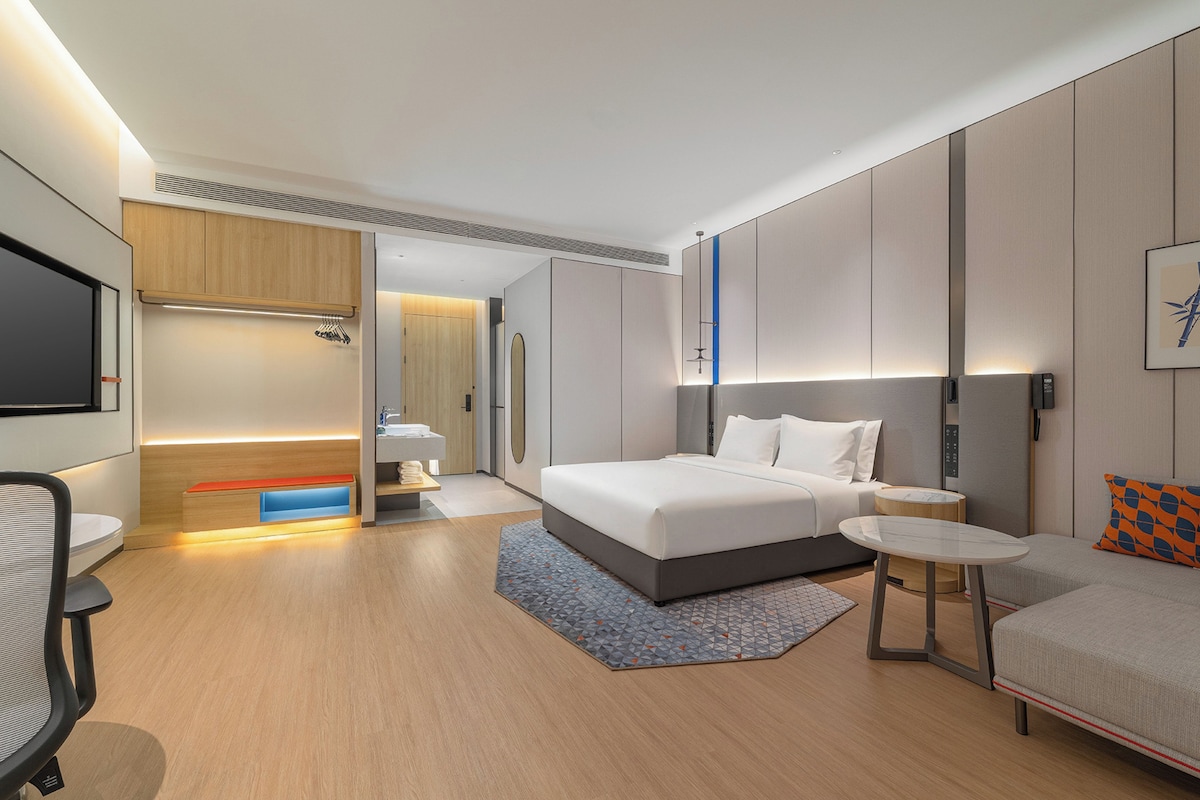 A modern hotel room with a bed, a desk, a chair, a small table, and a sofa.