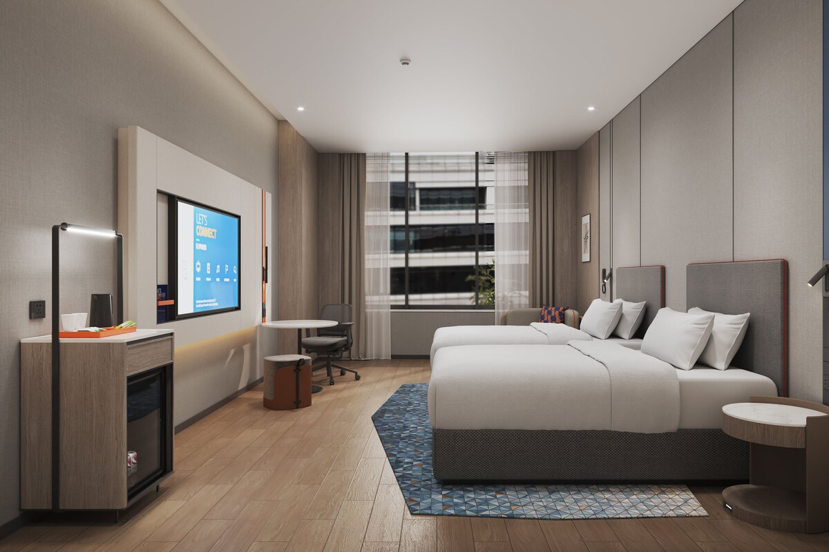 A modern hotel room with a bed, bedside tables, a desk, a chair, a TV, and a window with curtains.