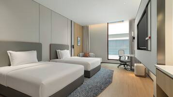 A hotel room with two beds, a desk, a chair, and a large window.