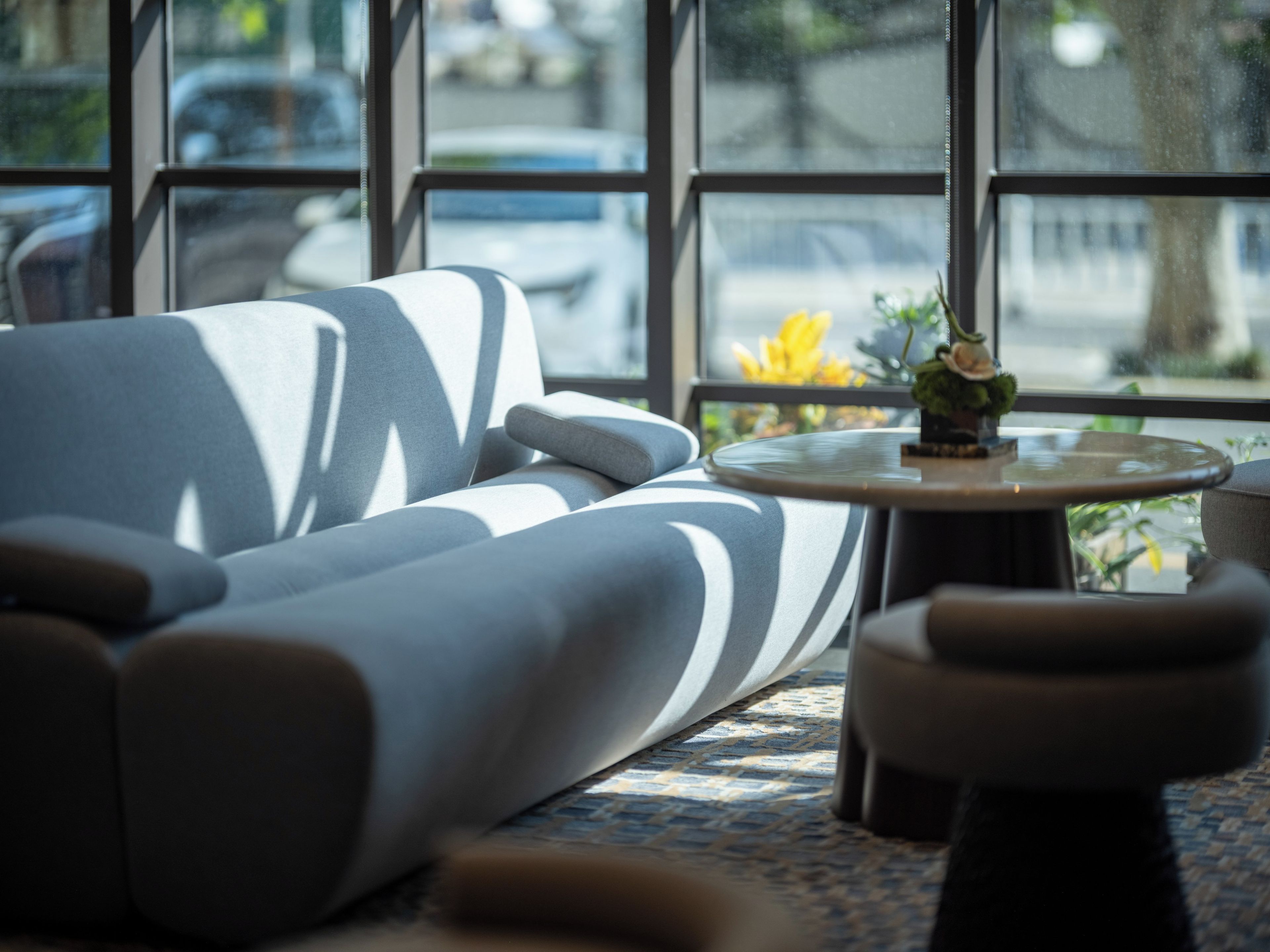 Ein modernes Interieur mit einer Couch und einem runden Tisch, große Fenster mit Blick auf die Straße.
