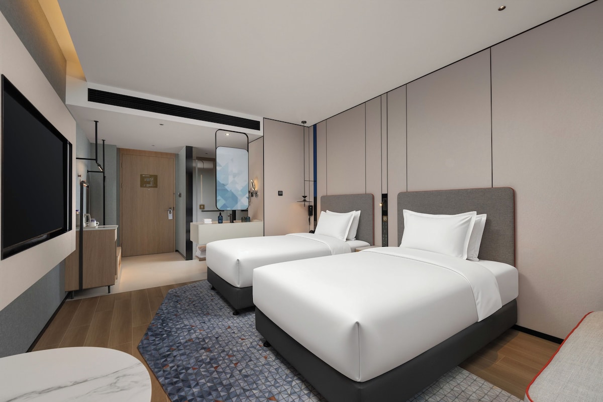 A hotel room with two beds, a bathroom, a TV, and a minibar.