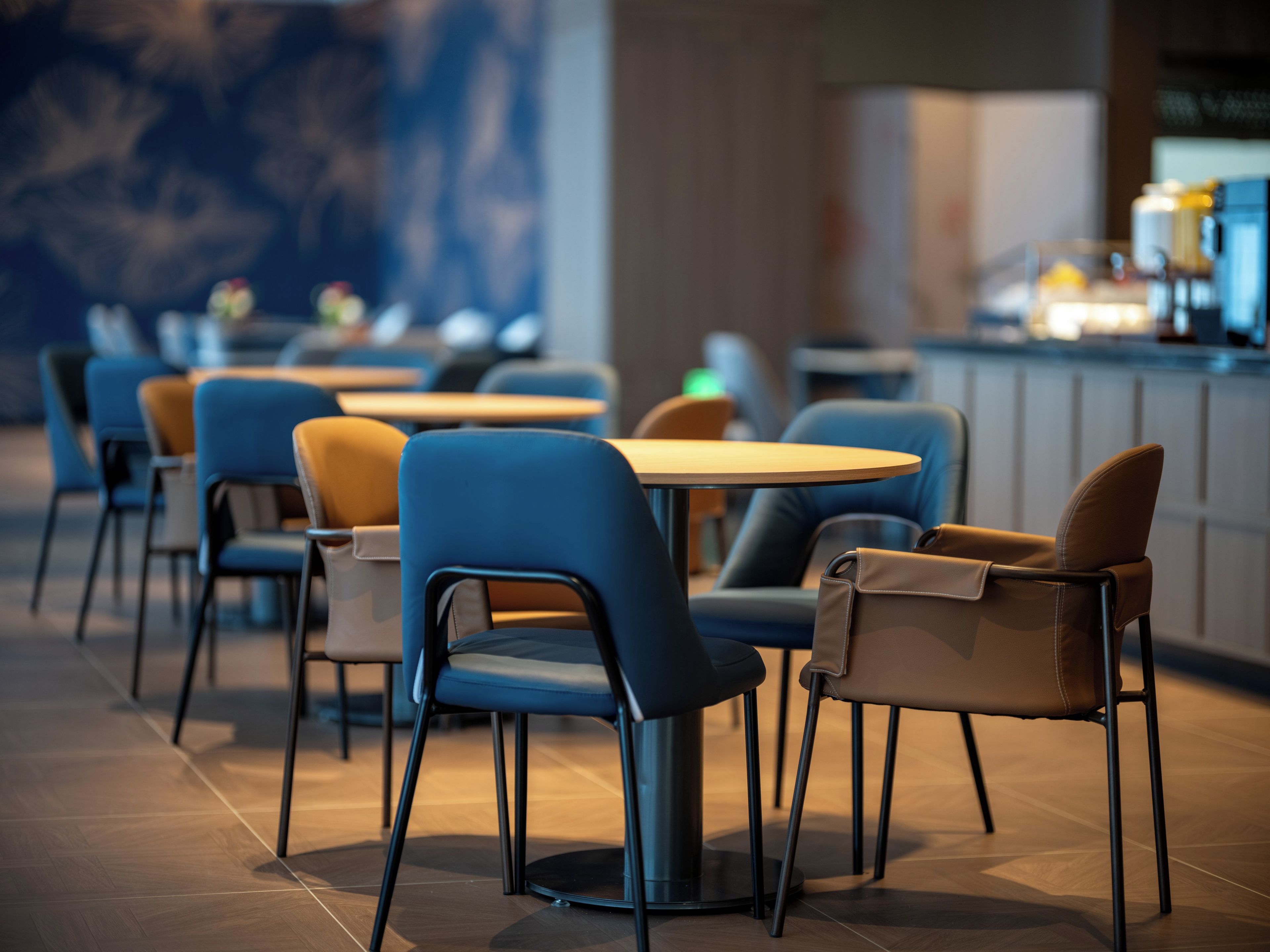 L’intérieur d’un restaurant moderne, avec des tables et des chaises rondes, un bar et un mur décoré d’un motif particulier en arrière-plan.