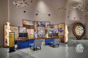 A reception desk with two chairs, a decorative wall with abstract art, and a unique illuminated sculpture.