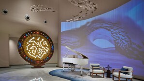 A modern interior with a grand piano, a large decorative wall, and a projection screen displaying a nature scene.