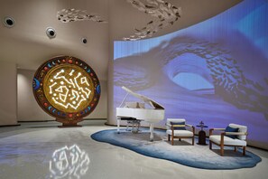 A modern interior with a grand piano, a large decorative wall, and a projection screen displaying a nature scene.