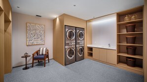 A laundry room with a chair, two washing machines, a sink, and shelves with baskets.