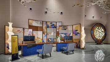 A reception desk with two chairs, a decorative wall with abstract art, and a unique illuminated sculpture.