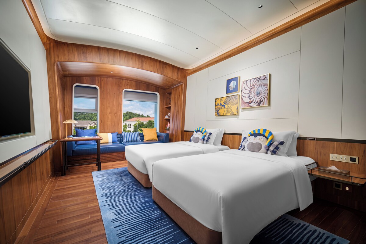 A hotel room with two beds, a sofa, a TV, and a window with a view.