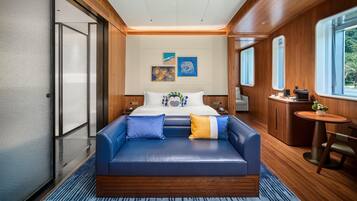 Una habitación de hotel moderna con una cama grande, un sofá azul, una mesita y vistas al exterior.