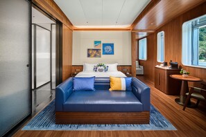 Ein modernes Hotelzimmer mit einem großen Bett, einem blauen Sofa, einem kleinen Tisch und Blick ins Freie.