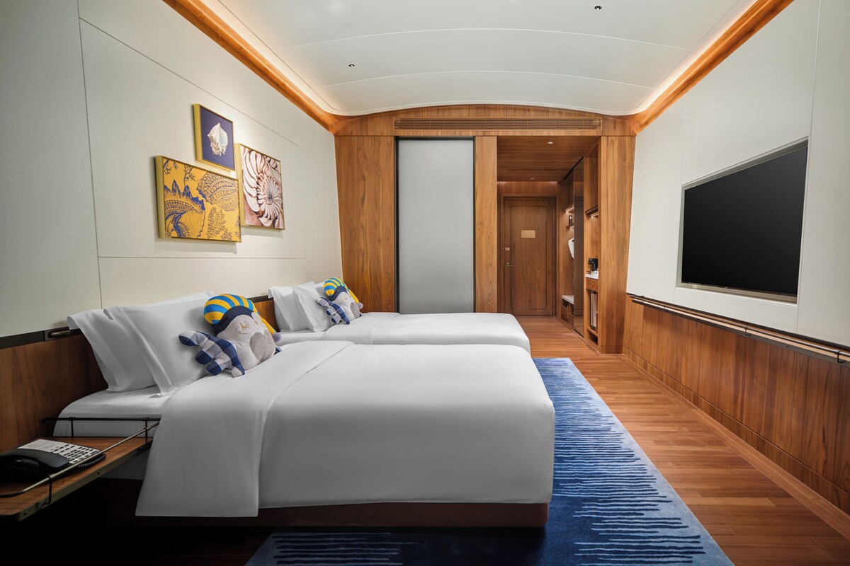 A hotel room with two beds, a flat-screen TV, artwork on the wall, and a wooden floor.