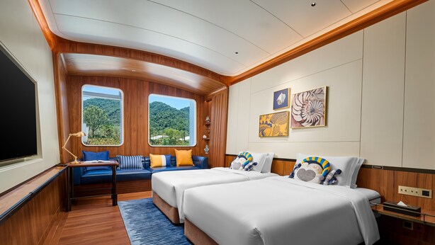 A cabin with two beds, a seating area, and a large window offering a view of the outdoors.
