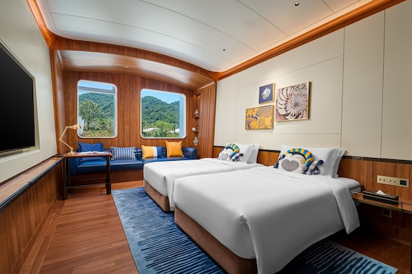 A cabin with two beds, a seating area, and a large window offering a view of the outdoors.