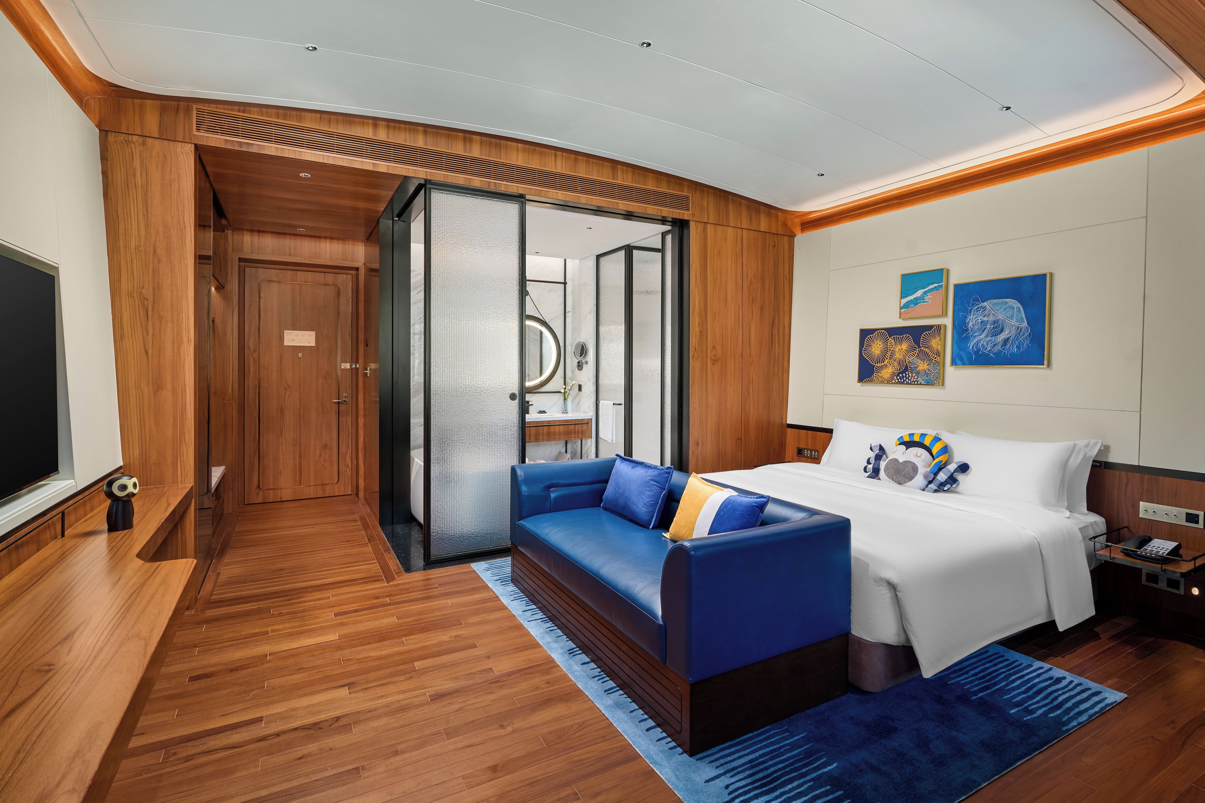 Una habitación de hotel moderna con piso de madera, un sofá azul, una cama con ropa de cama blanca y obras de arte en la pared.