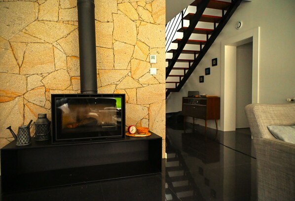 A modern living room with a stone wall, a black fireplace, and a staircase leading to an upper level.