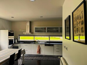 A modern kitchen with a dining area, a built-in oven, and a window with a view of a green field.