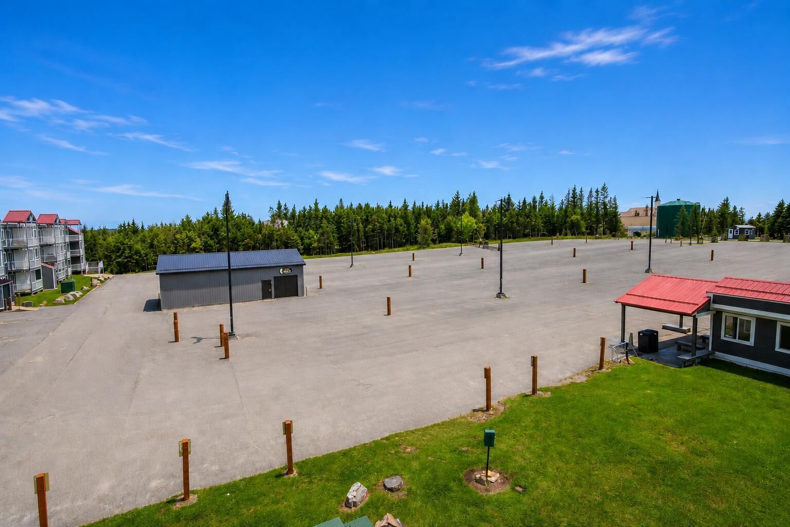 A large parking lot with a small building, surrounded by trees and a few residential buildings.