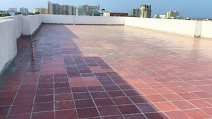 A rooftop terrace with red tiles, a white wall, and a view of a cityscape.