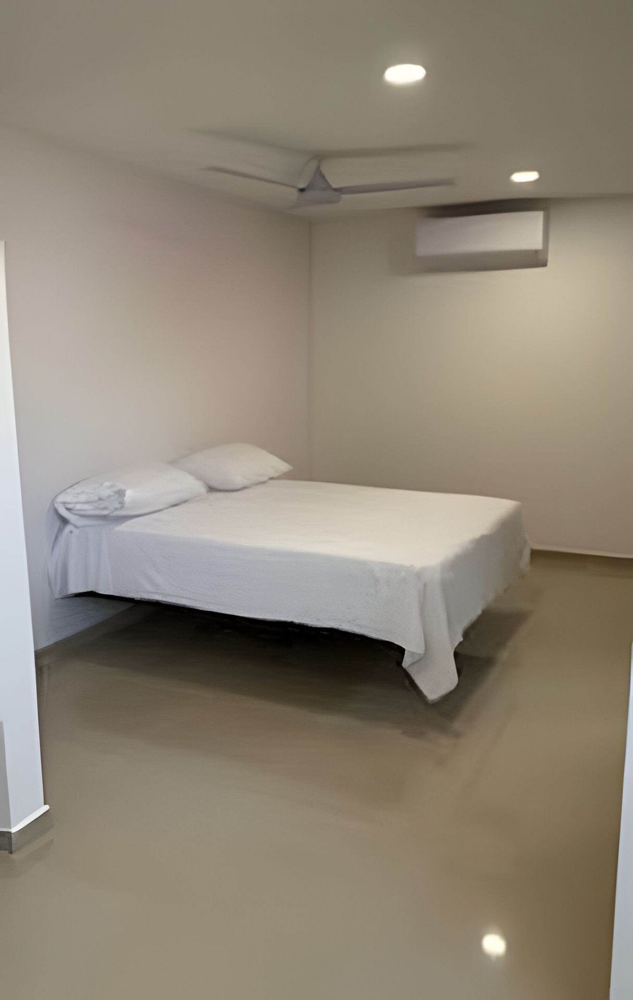 Habitació individual amb un ventilador de sostre, il·luminació empotrada i paret blanca.