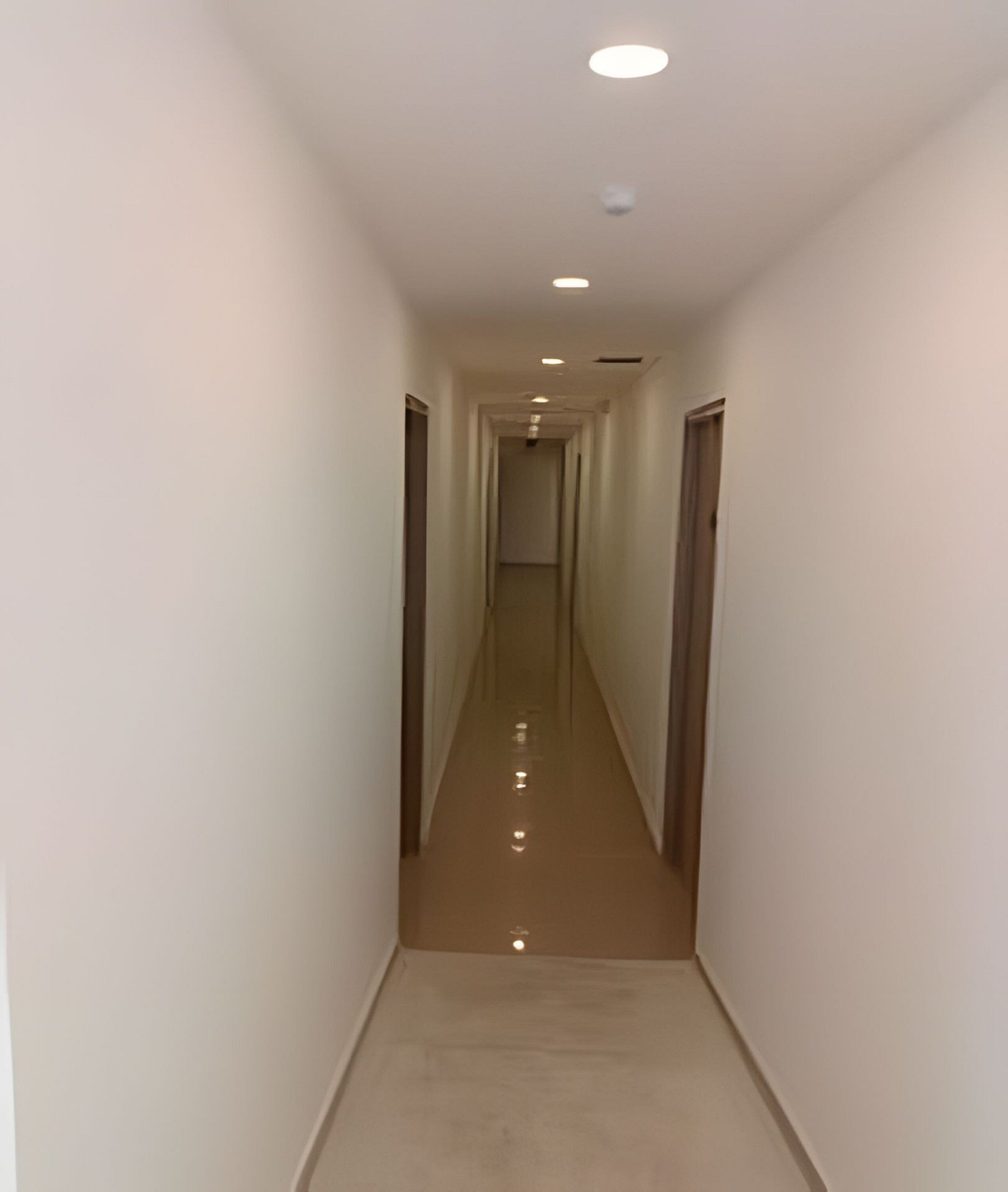 Un pasillo estrecho y bien iluminado con piso reflectante, que conduce a una puerta al final.