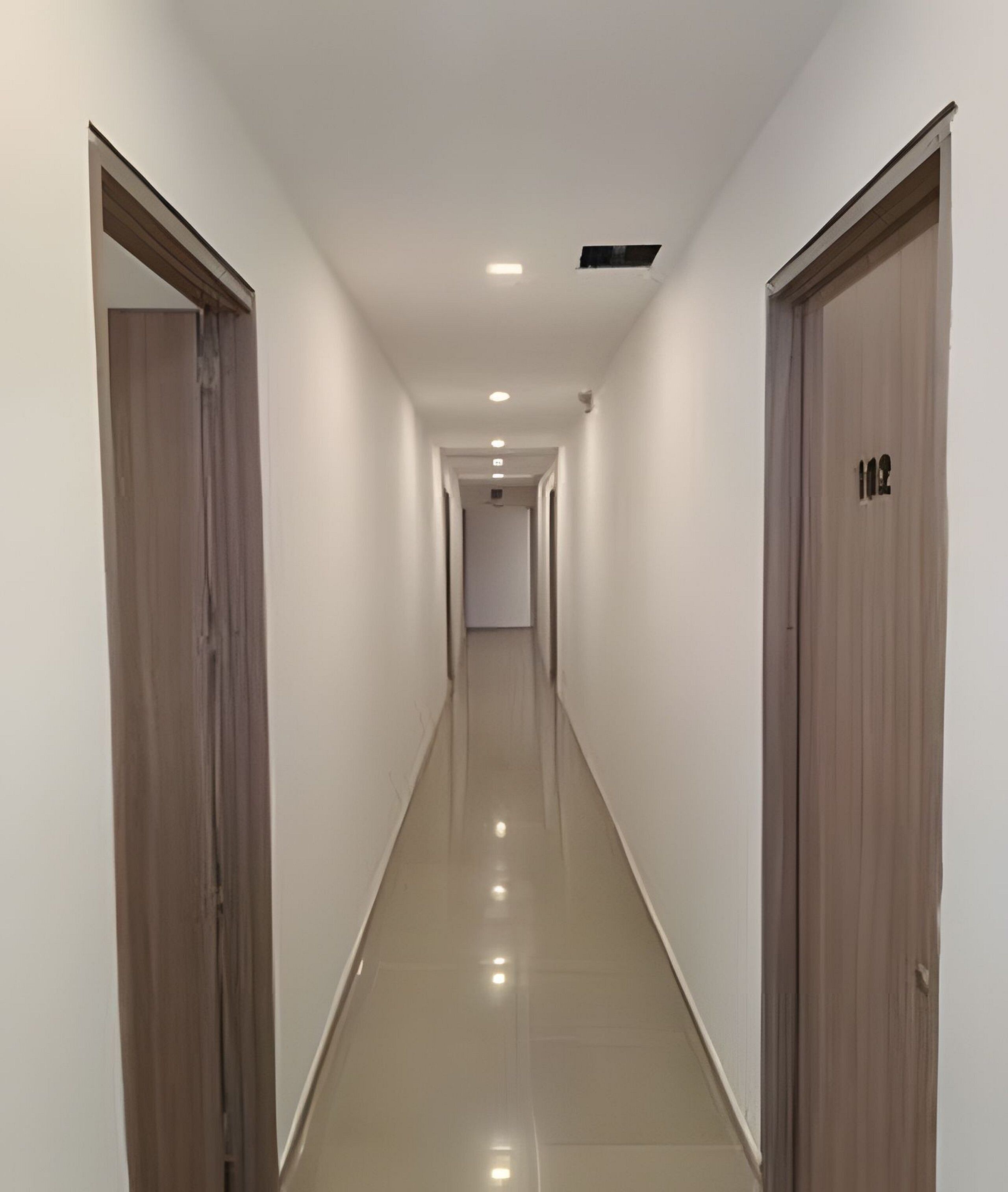 A long, narrow hallway with wooden doors on either side and a shiny tiled floor.