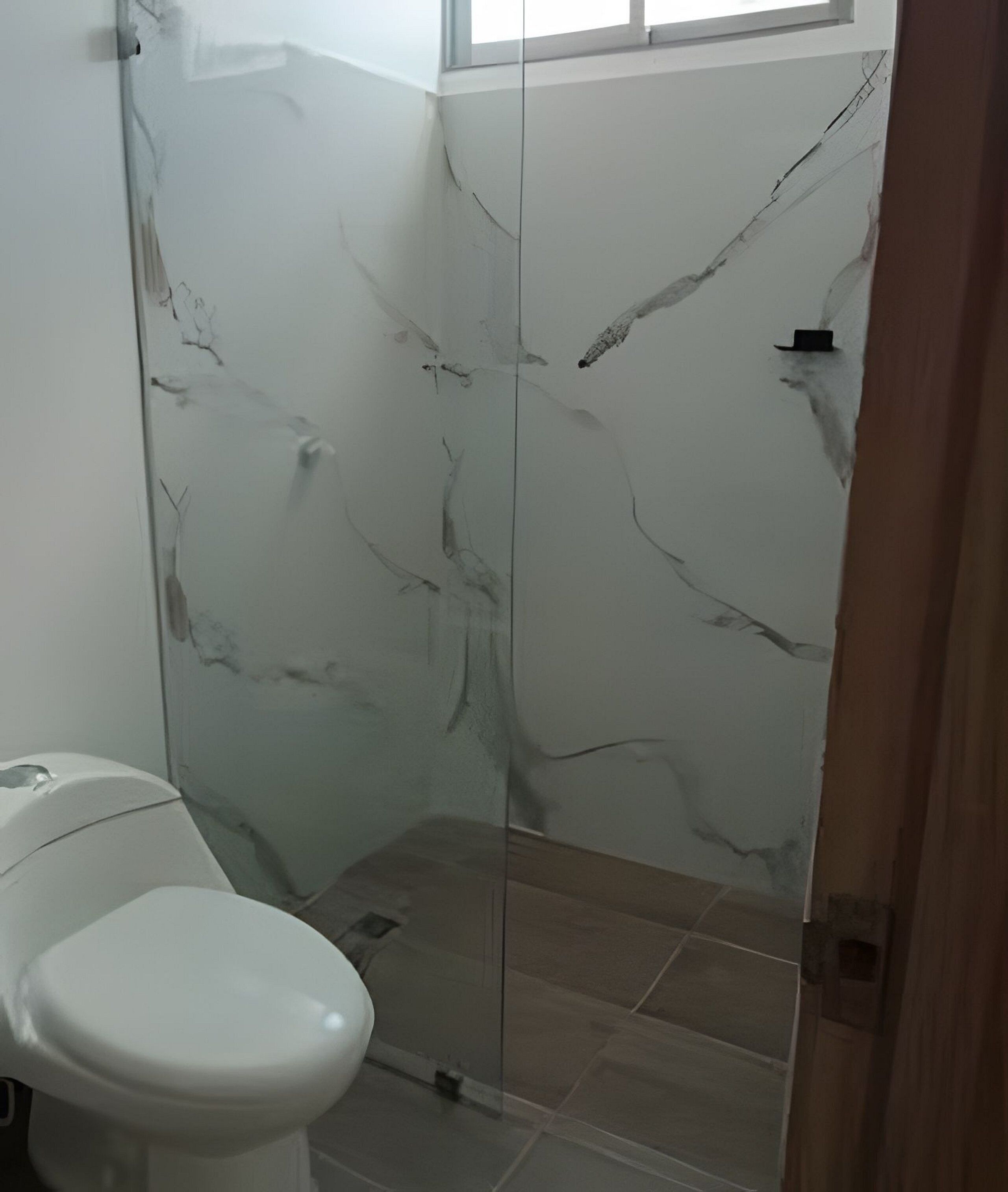 A bathroom with a toilet, a shower enclosure with marble walls, and a window above the shower.