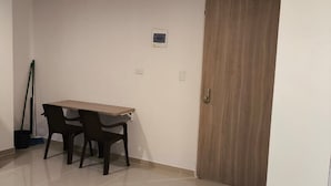 A room with a wooden table and chairs, a door, and a light switch on the wall.