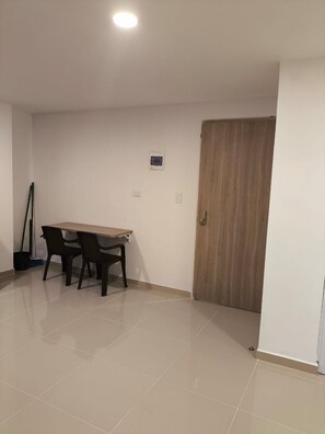 Una habitación con una mesa y sillas de madera, una puerta y un interruptor de luz en la pared.