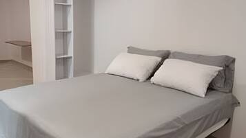 A minimalist bedroom with a bed, two pillows, and a white wardrobe.