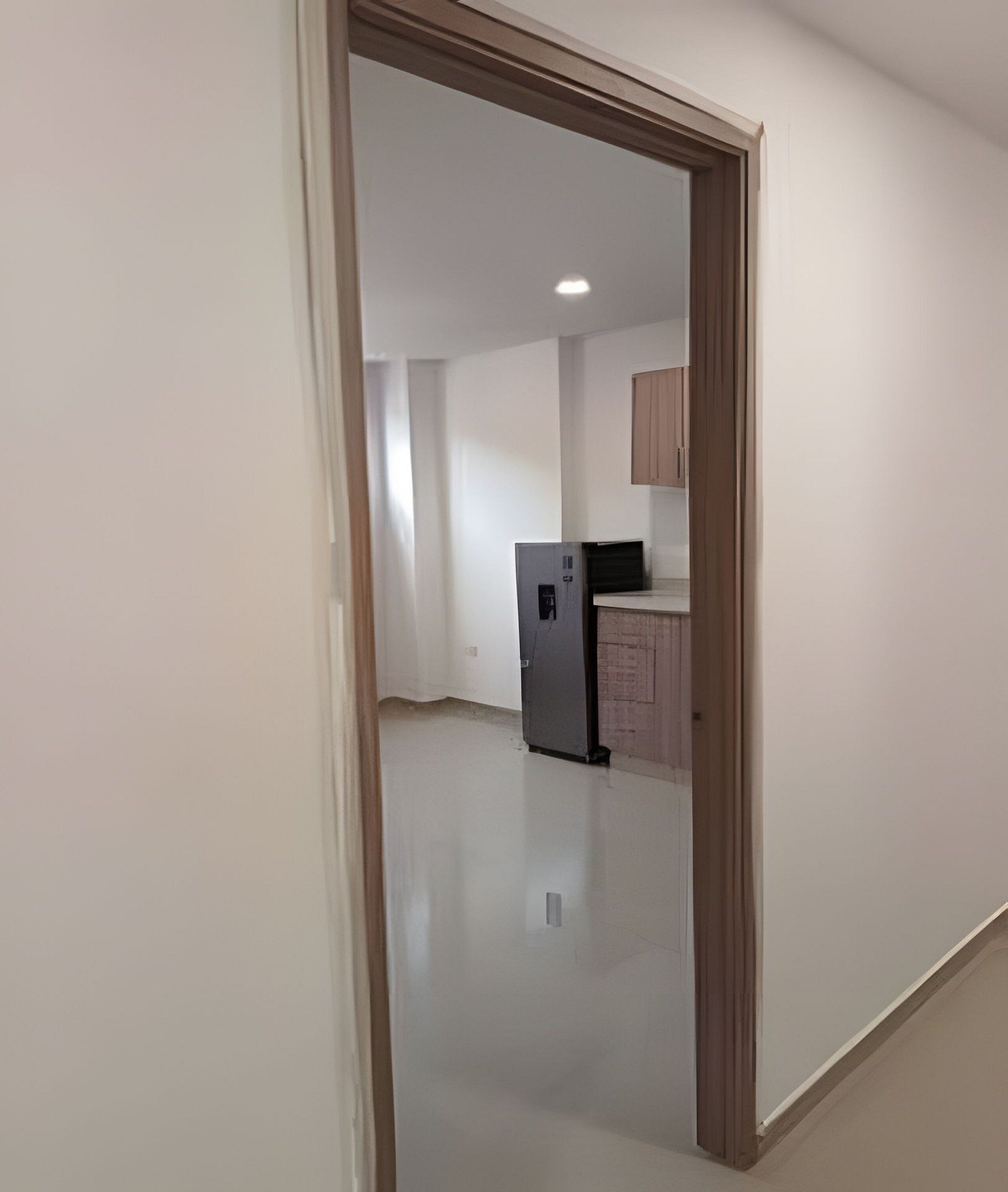 An interior view of a hallway leading to a kitchen area with a refrigerator and cabinets.