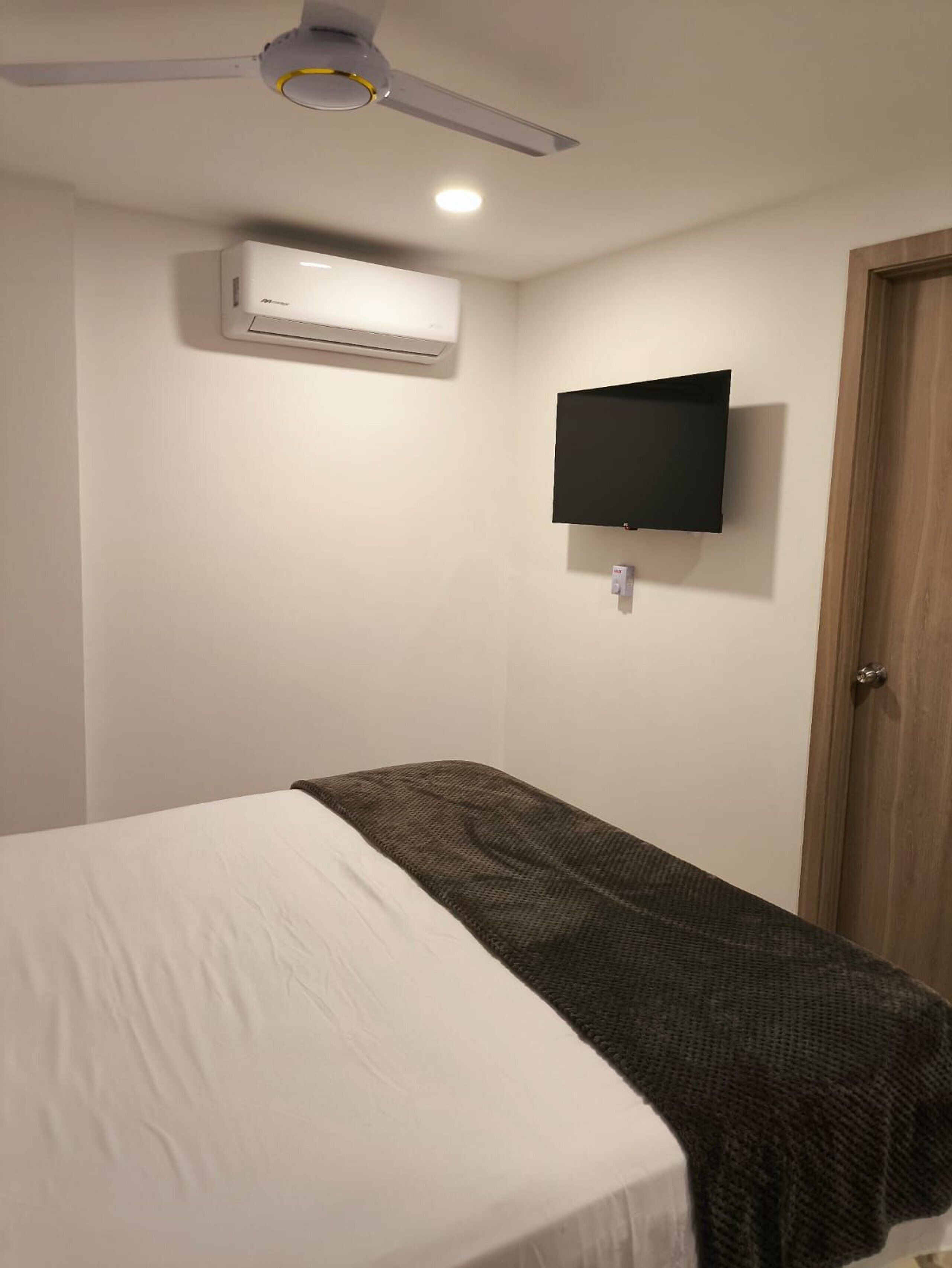 Um quarto com uma cama, televisão na parede, ar condicionado e ventilador de teto.