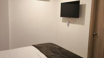 Um quarto com uma cama, televisão na parede, ar condicionado e ventilador de teto.