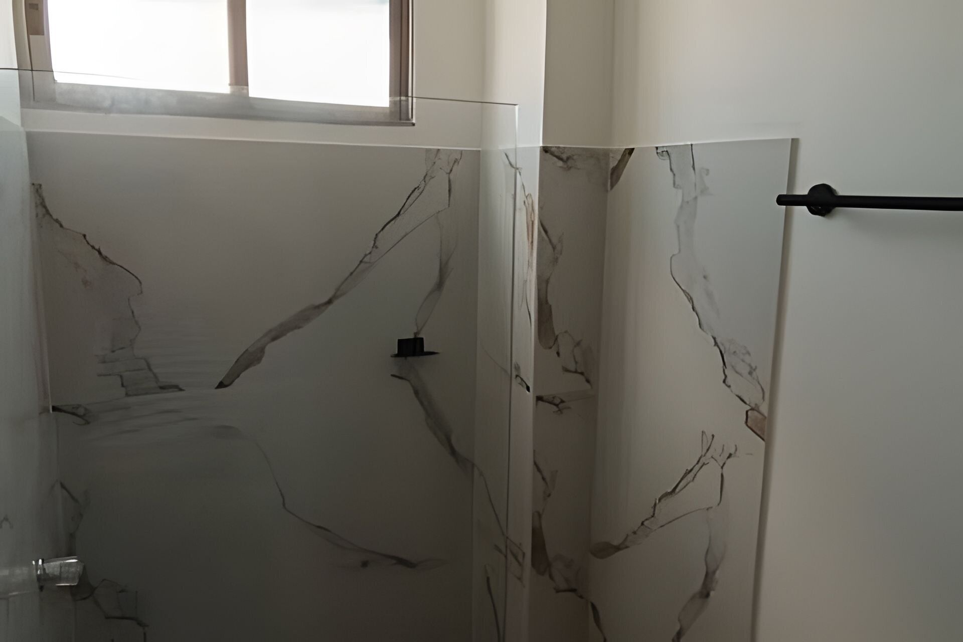 Un baño con pared de mármol y un perchero negro.