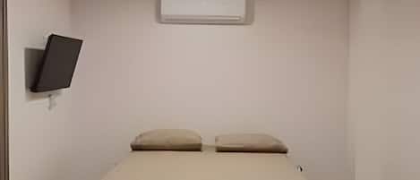 A bedroom with a bed, an air conditioning unit, a ceiling fan, and a wall-mounted television.