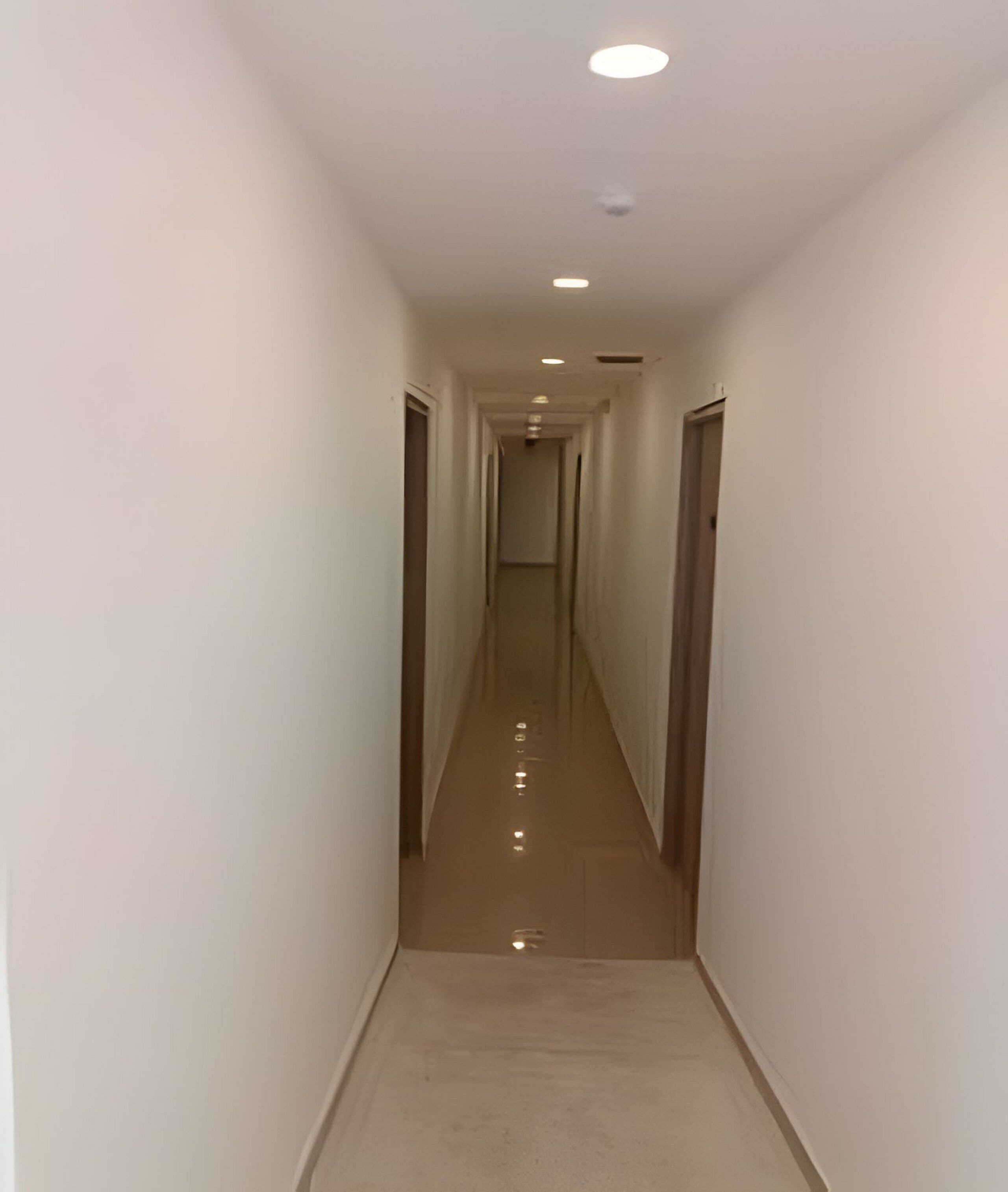Un pasillo estrecho y bien iluminado con piso reflectante, que conduce a una puerta al final.